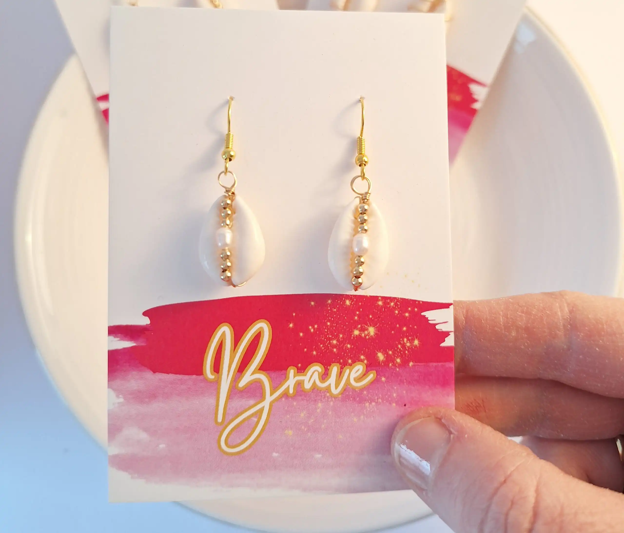 Hängende Perlenohrringe auf weißer Karte mit "Brave" Schriftzug, Schmuck, Accessoire, Geschenk.