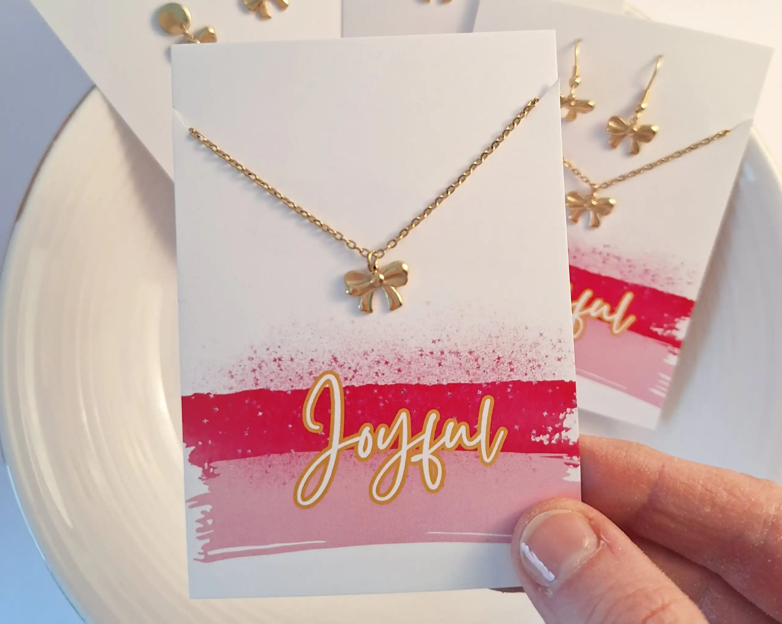 Ein Schmuckset mit goldener Kreuz-Halskette und Ohrringen auf einer Grußkarte mit "Joyeux" Schriftzu.