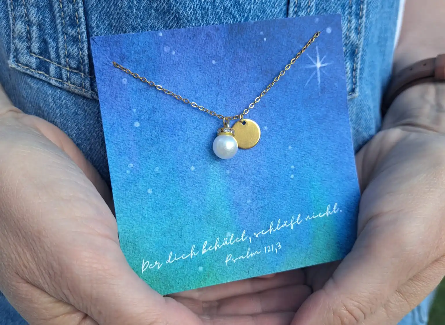 Der christliche Schmuck mit Perle und goldener Medaille auf blauer Himmelkarte.