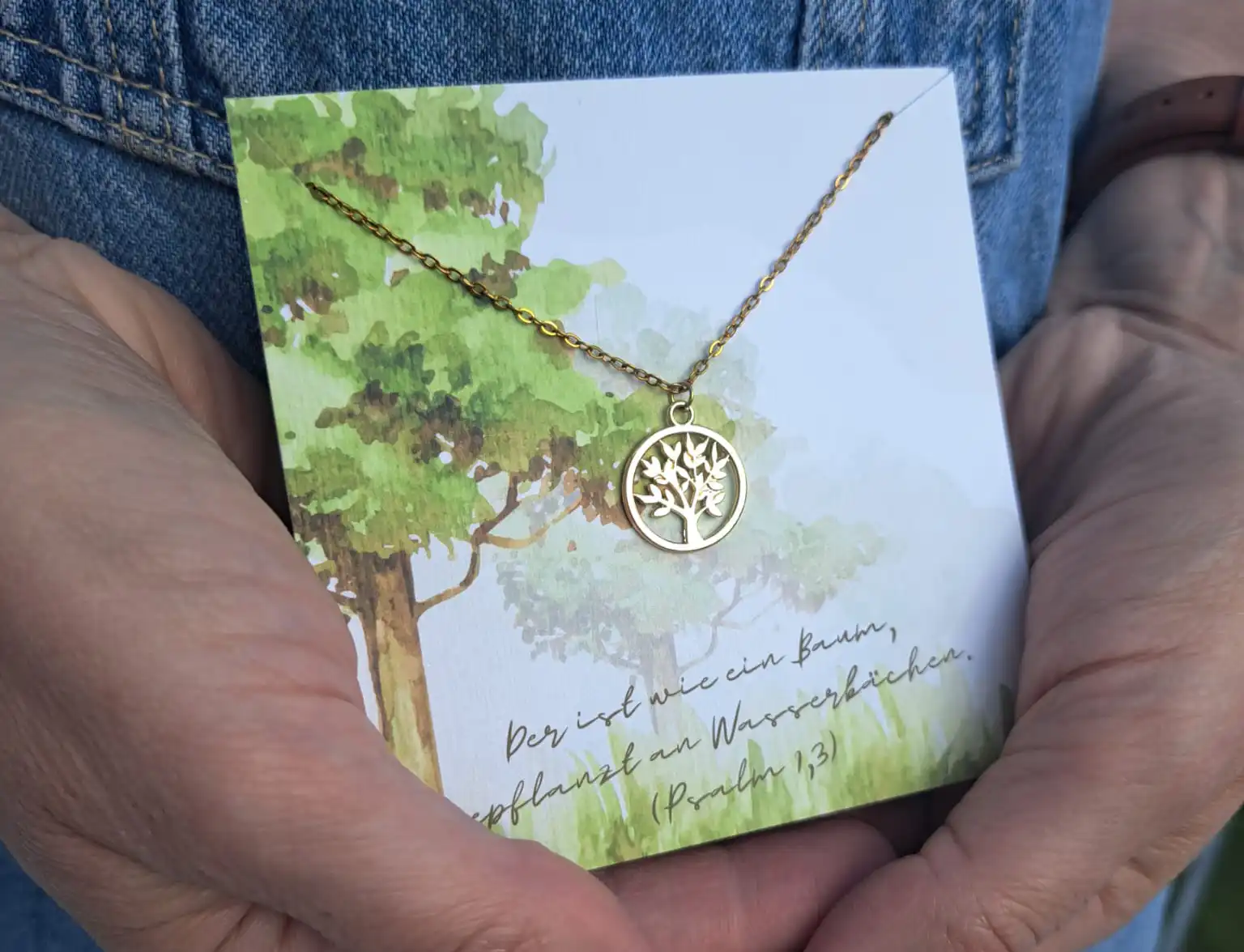 Der goldene Baum-Anhänger auf einer Grußkarte mit Baumillustration, symbolisiert Natur und Glauben.