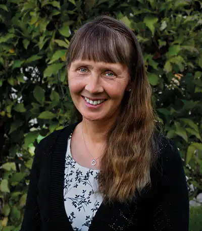 Ein freundliches Porträt einer Frau vor grüner Natur, geeignet für christliche Marken.