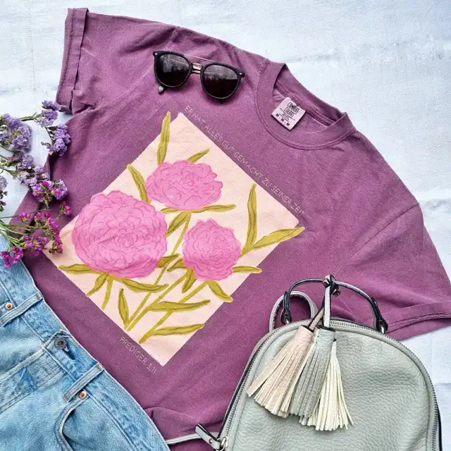 Shirt - Er hat alles gut gemacht 1 Ein stilvolles lila T-Shirt mit Blumenmuster, Sonnenbrille und Handtasche, christliche Mode.