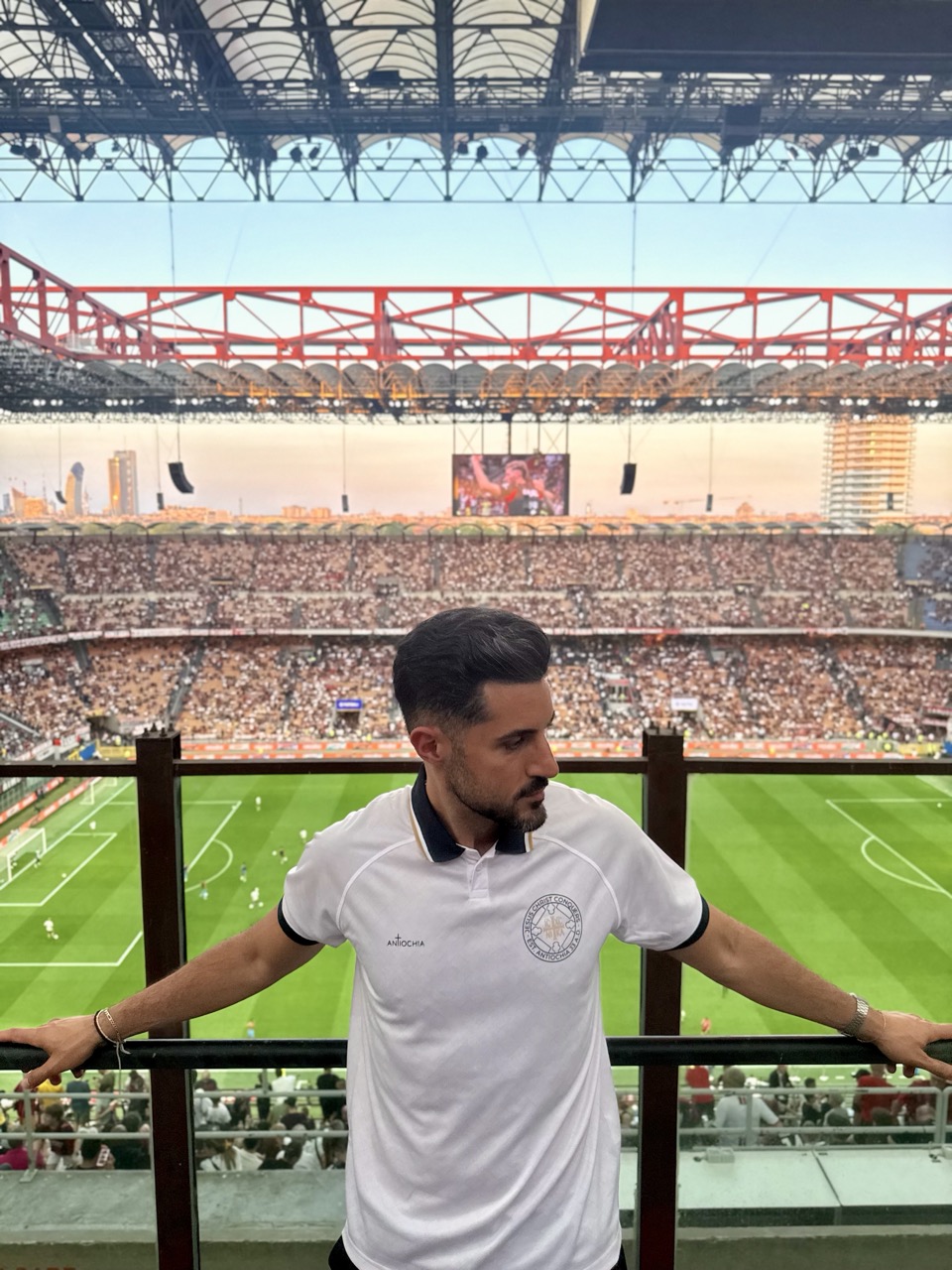 Sieger-Trikot - "Jesus Christ conquers" 5 Fußballstadion mit einem Mann in weißem Trikot, Blick auf das Spielfeld, große Zuschauerzahl.