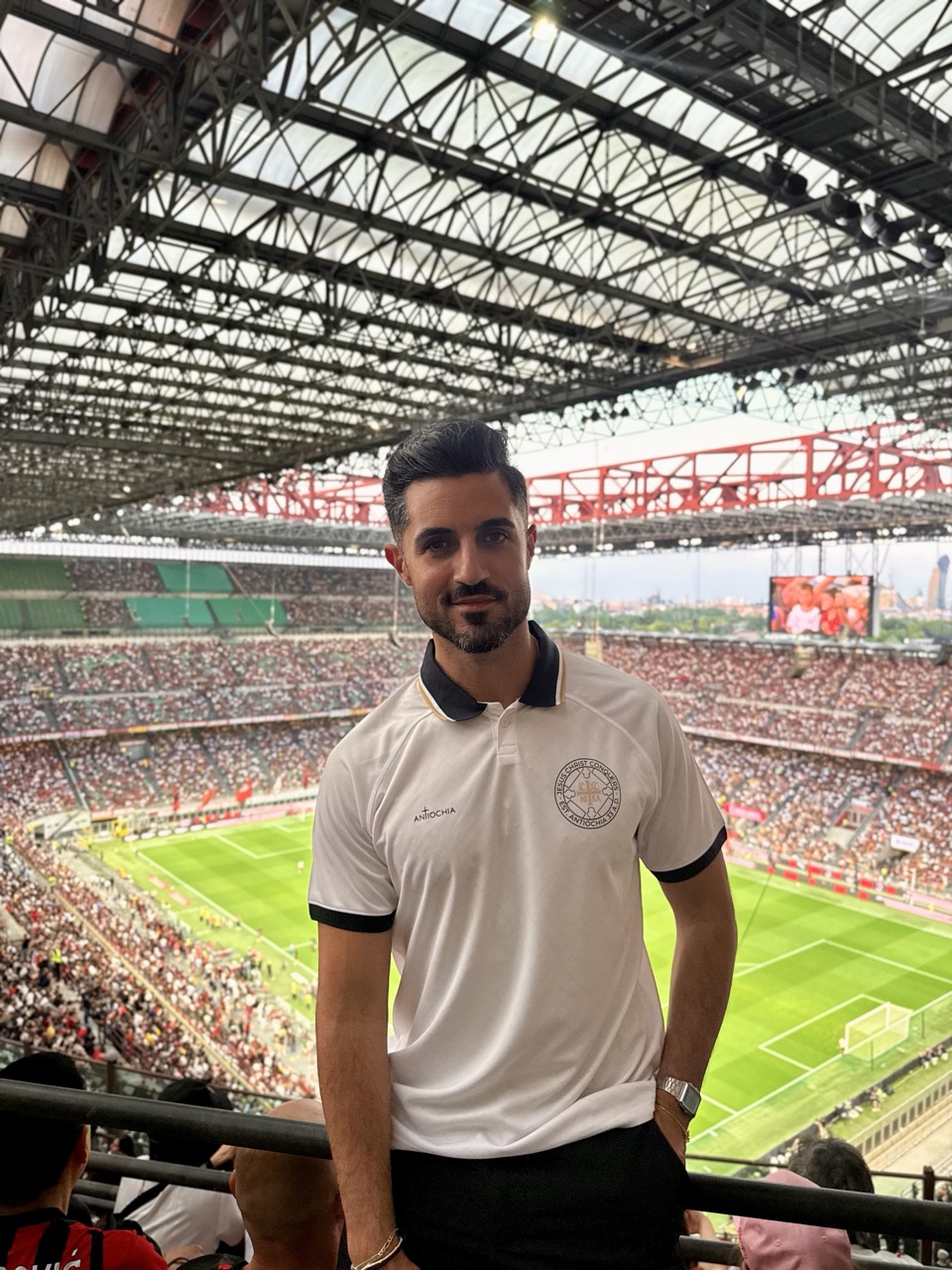 Sieger-Trikot - "Jesus Christ conquers" 3 Der Mann im Stadion trägt ein weißes T-Shirt mit christlichem Logo, Blick auf das Fußballfeld.