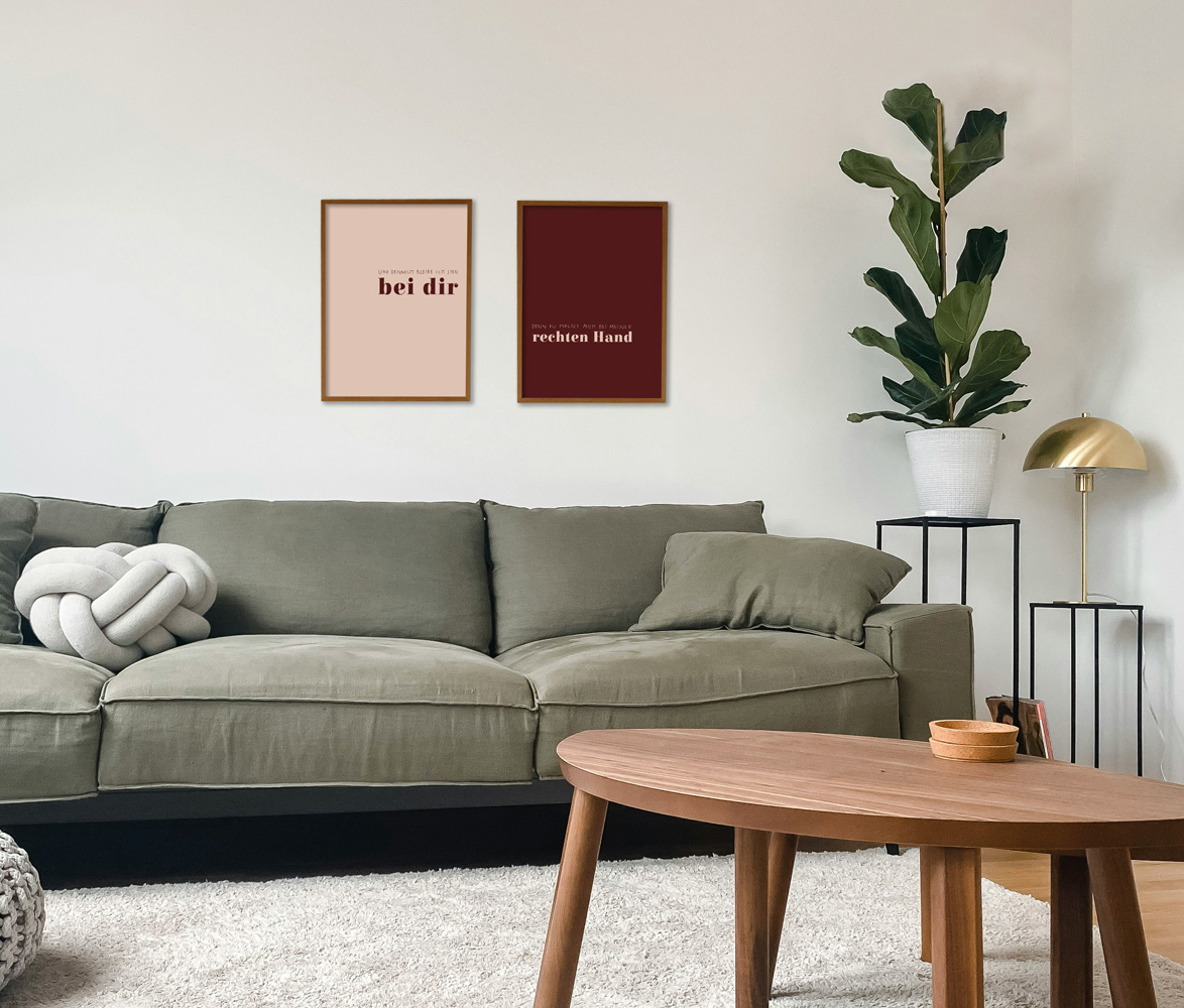 POSTER-DUO "UND DENNOCH" 2 Ein modernes Wohnzimmer mit grauem Sofa, Pflanzen und dekorativen Bildern, stilvoll eingerichtet.