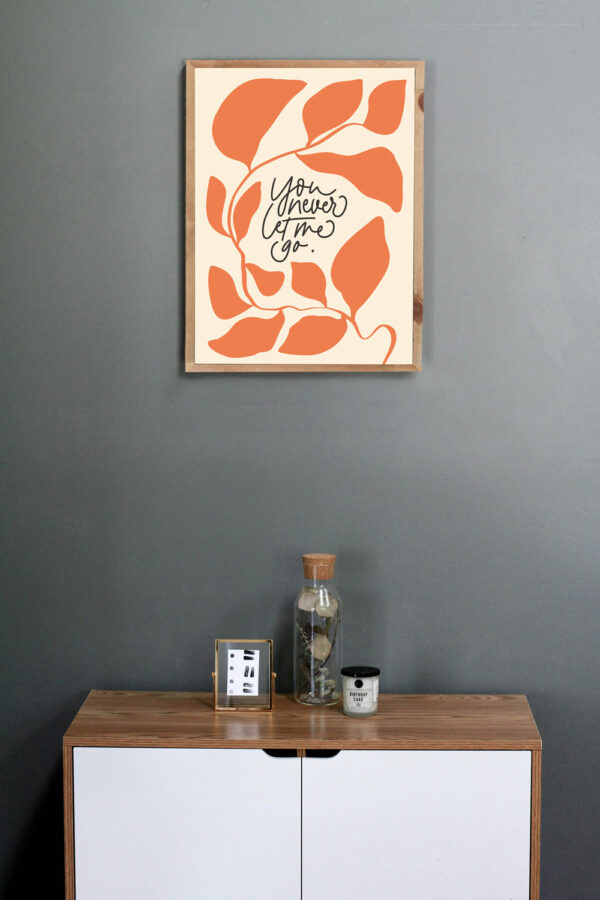 Der Spruch "You Never Lome to Go" auf einem modernen Wandbild in warmen Orangetönen, über einem Holz.