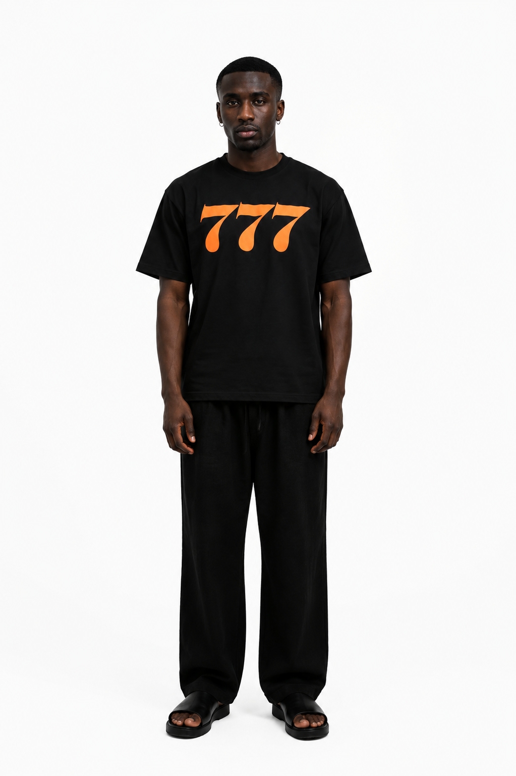 Dunkelhäutiger Mann trägt schwarzes T-Shirt mit orange 777-Logo und schwarze Hosen.