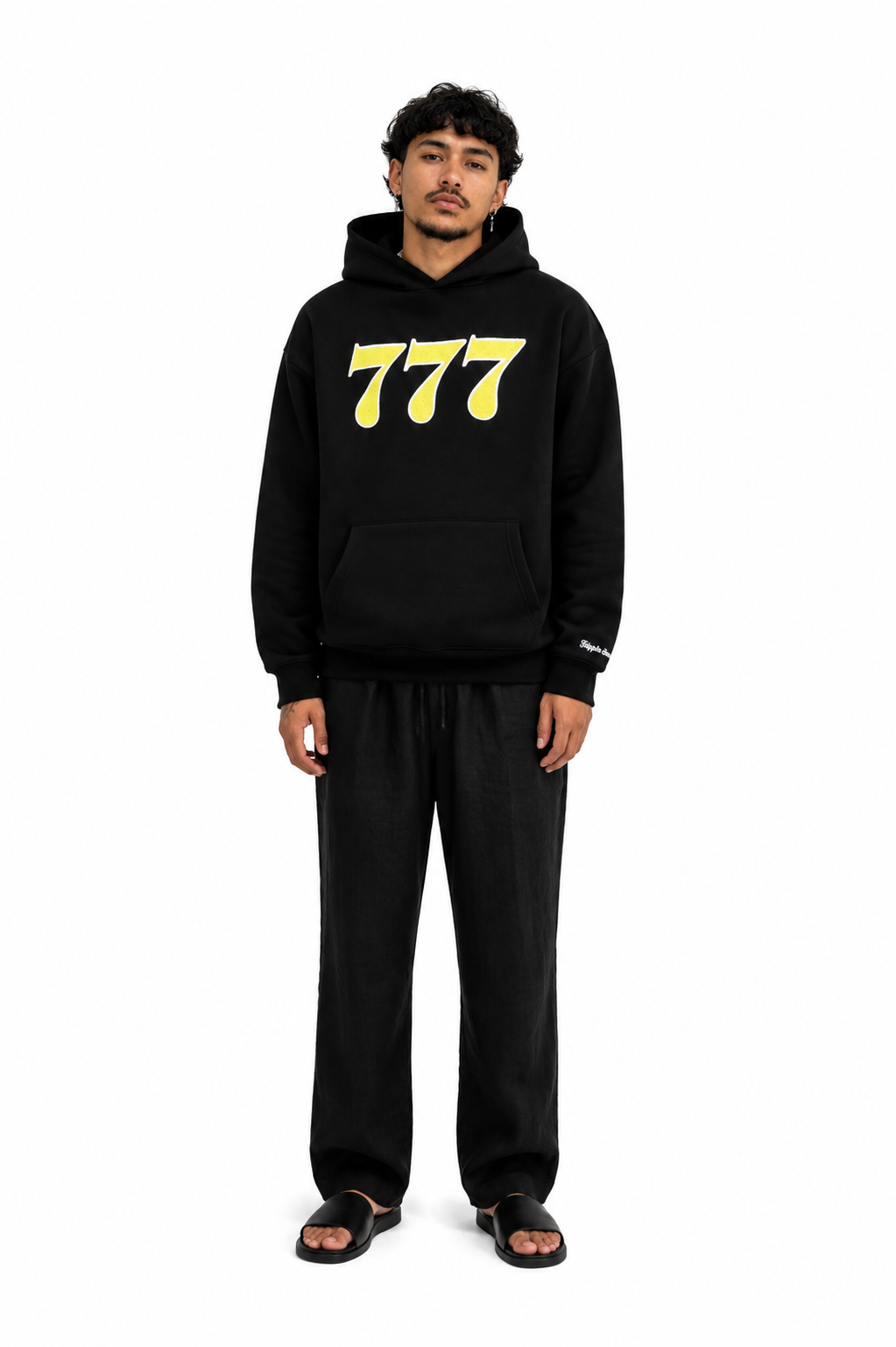 Moderner junger Mann trägt schwarzen Hoodie mit gelben "777" Zahlen, lässiger Stil.