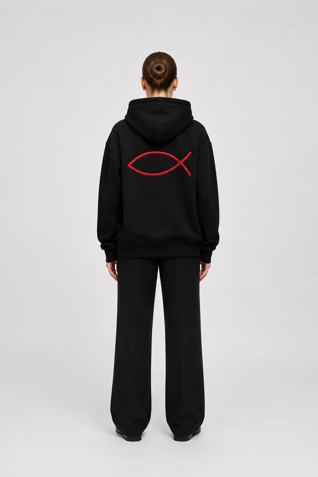 Ein Mensch trägt eine schwarze Kapuzenjacke mit rotem Fischsymbol, symbolisch für Christentum.
