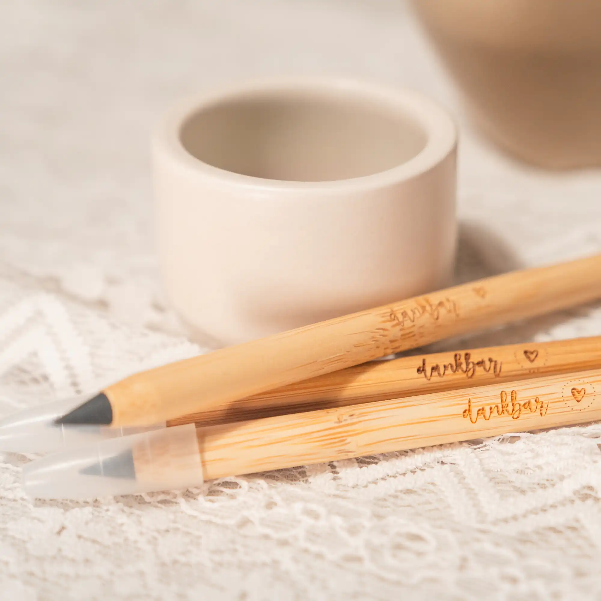 Unendlichkeitsstift 1 Zwei Dankbarkeitsstifte neben einer weißen Keramikschale auf Spitze-Tuch.