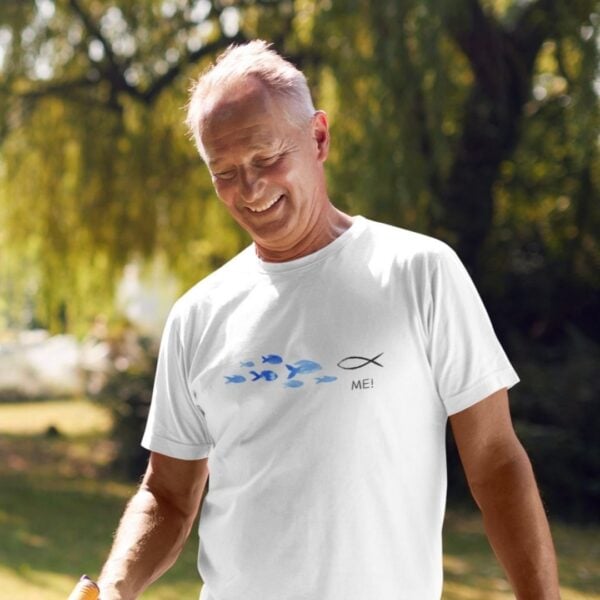 Ein älterer Mann trägt ein weißes T-Shirt mit Fisch-Design und christlichem Text, im Park.