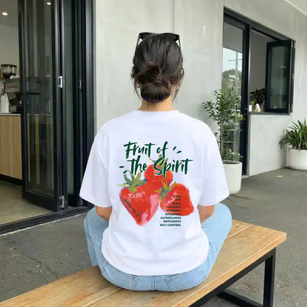 Person trägt T-Shirt mit Herz-Design und spirituellen Motiven vor modernem Gebäude.