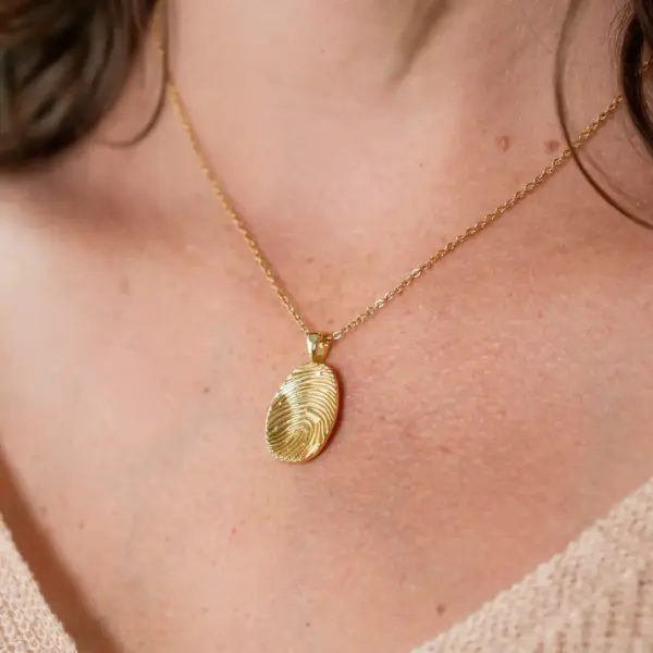 Goldenes Halskettchen mit Fingerabdruck-Anhänger vor heller Haut.