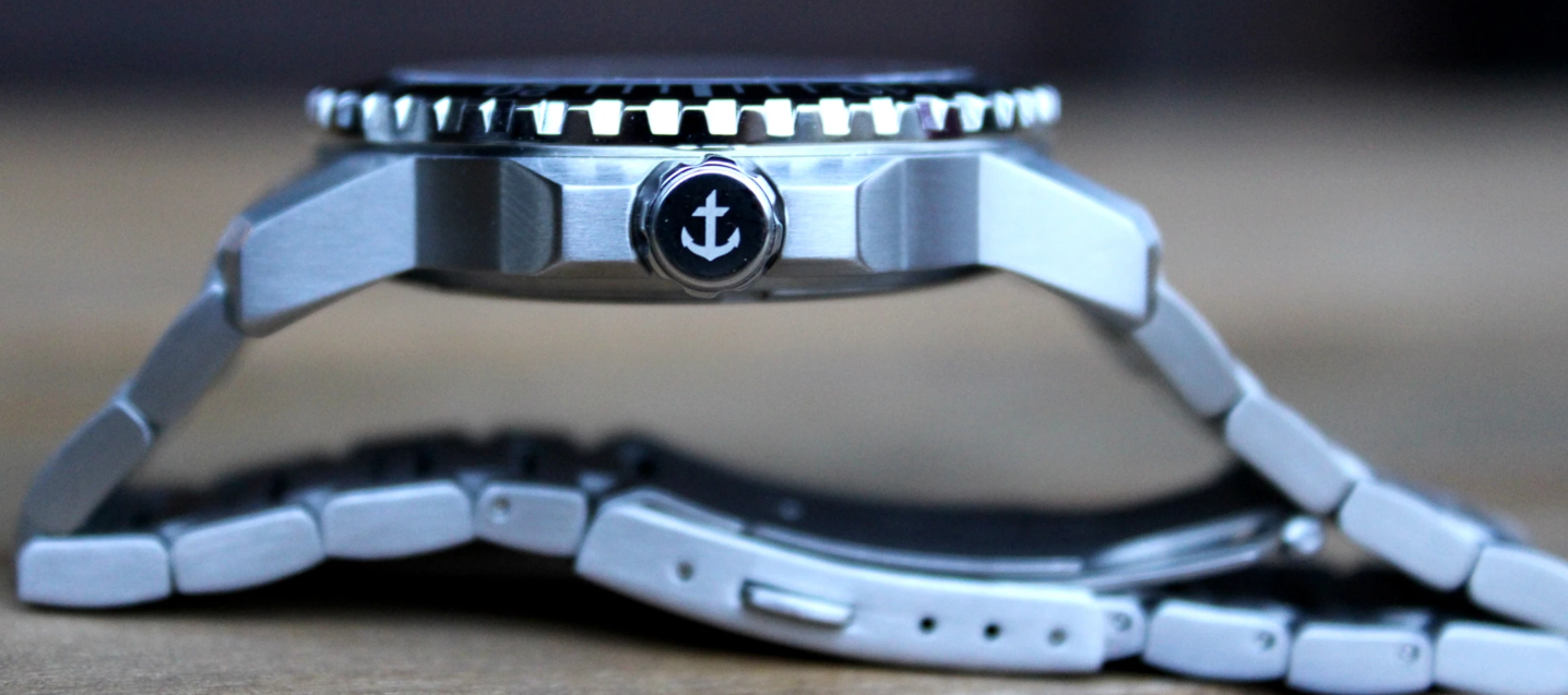 OCEAN OF FAITH - Schweizer Uhr inspiriert vom Glauben - Schwarz Edelstahl 6 Nahaufnahme einer silbernen Armbanduhr mit Anker-Logo auf der Lünette.