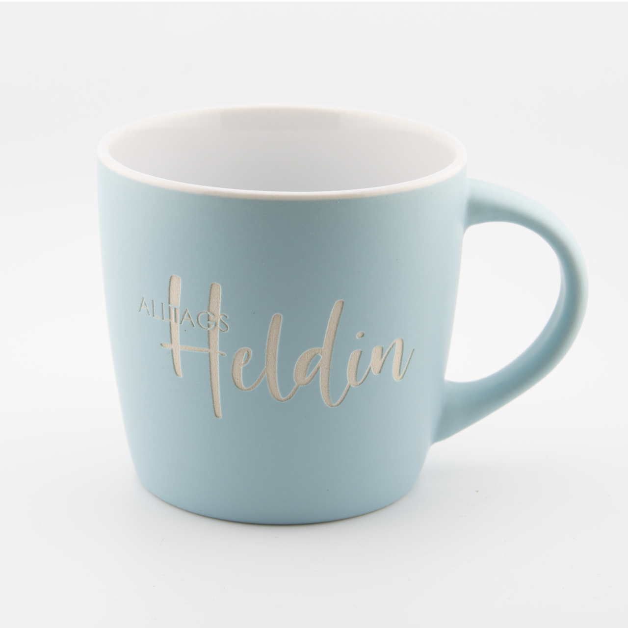Hellblaue Tasse mit goldener Beschriftung 'Alltags Heldin' auf weißem Hintergrund.