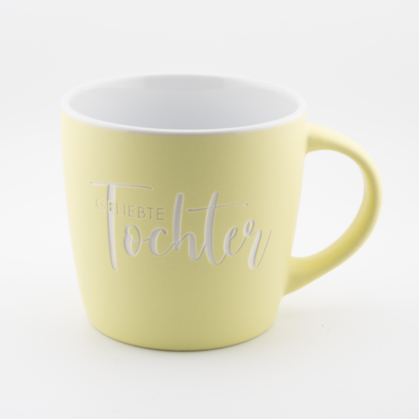 Gelbe Tasse mit christlichem Spruch 'Glaubte Tochter' auf weißem Hintergrund.