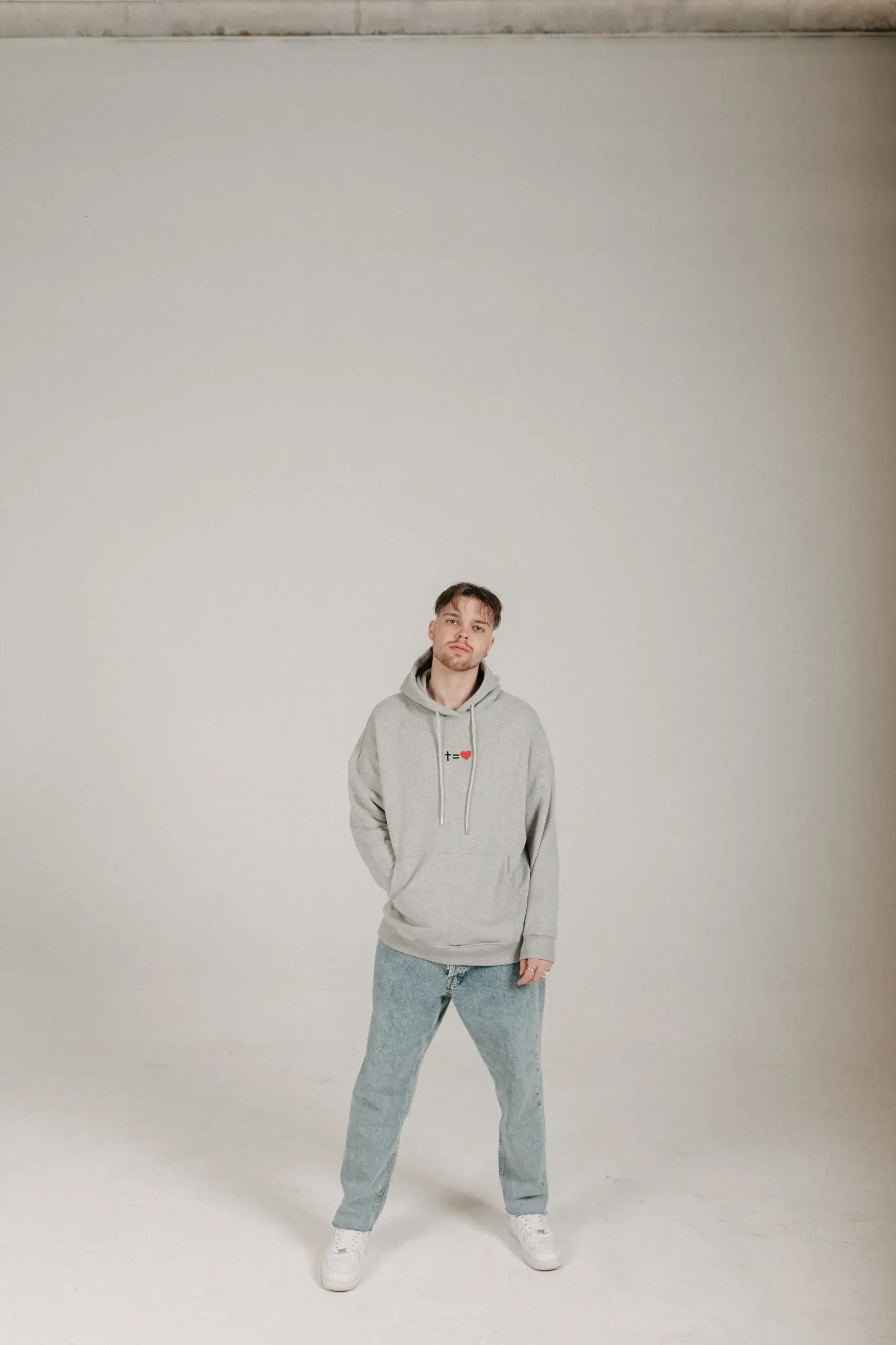 kreuzgleichliebe Hoodie Style Gratitude - unisex 21 Junger Mann trägt grauen Hoodie mit christlichem Motiv und blauen Jeans.