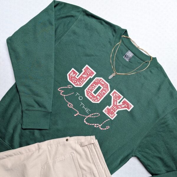 Grüner Pullover mit 'Joy to the World'-Print und goldener Kette.
